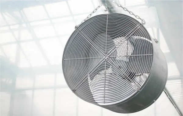 A close-up of a stainless steel industrial air circulation fan with a protective wire cage and large black blades, designed for high-efficiency ventilation